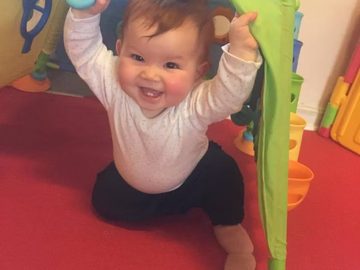 A smiling toddler reaching up during play at Kidz R Os
